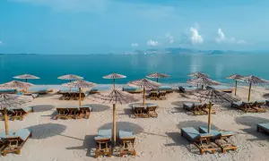 Puste leżaki i parasole na piaszczystej plaży, idealne na spokojny wypoczynek. W tle błękitne morze i góry.
