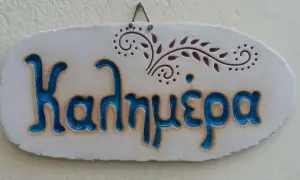 Ceramiczna tabliczka z napisem "Kalimera", czyli "cześć po grecku", ozdobiona delikatnym wzorem.