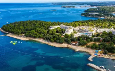 Hotel Delfin Plava Laguna, otoczony zielenią, z basenami i plażą nad turkusowym morzem. Idealne miejsce na wakacje.