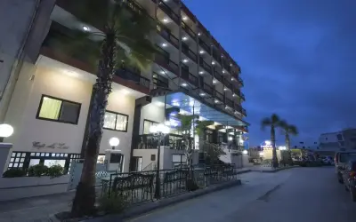 Hotel Canifor Malta o zmierzchu, z palmami i oświetlonymi balkonami.