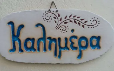 Ceramiczna tabliczka z napisem "Kalimera", czyli "cześć po grecku", ozdobiona delikatnym wzorem.