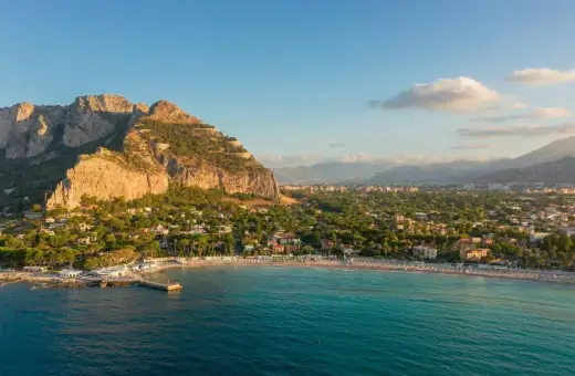 Malowniczy widok na Mondello Beach z turkusową wodą, piaszczystą plażą i górami w tle.