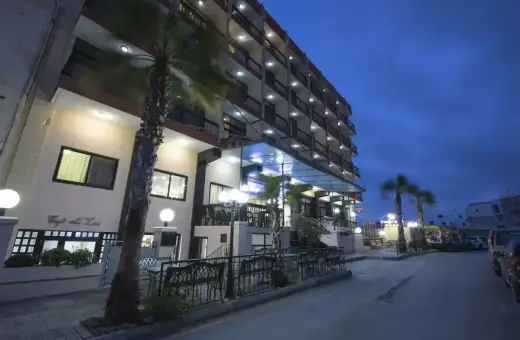 Hotel Canifor Malta o zmierzchu, z palmami i oświetlonymi balkonami.