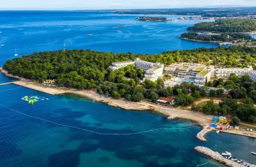 Hotel Delfin Plava Laguna, otoczony zielenią, z basenami i plażą nad turkusowym morzem. Idealne miejsce na wakacje.