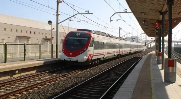 Nowoczesny pociąg Renfe z czerwonym przodem stoi na stacji. W tle budynek i peron.