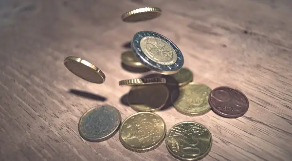 Monety euro spadające na drewniany blat. To waluta Hiszpanii, symbolizująca bogactwo i handel.