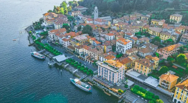Urokliwe como miasto nad jeziorem, z kolorowymi budynkami, zielenią i łodziami przy nabrzeżu.