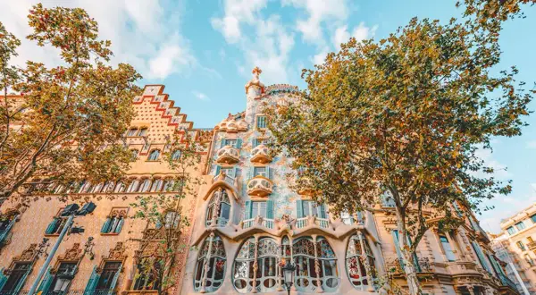 Piękna pogoda w Barcelonie w listopadzie. Drzewa wokół Casa Batlló mienią się jesiennymi barwami, a niebo jest błękitne.