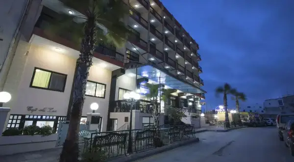 Hotel Canifor Malta o zmierzchu, z palmami i oświetlonymi balkonami.
