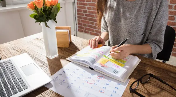Kobieta planuje spotkania i zadania w kalendarzu, przygotowując się do święta po ramadanie. Na biurku laptop, róże i okulary.