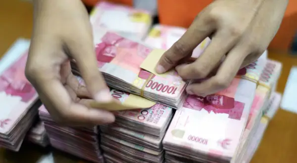 Ręce liczą stosy banknotów 100 000 rupii, waluta Indonezji.