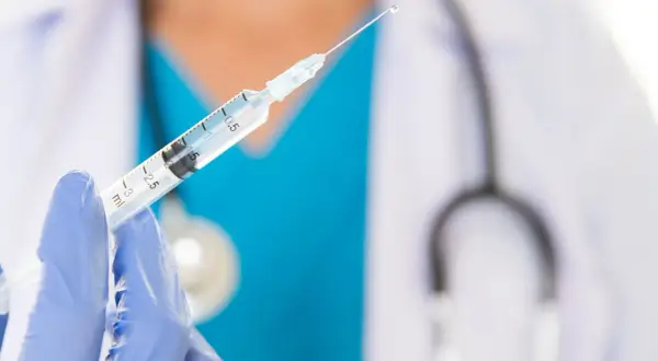 Lekarz w niebieskiej rękawiczce trzyma strzykawkę z kroplą szczepionki. Dostępne są szczepienia na Sri Lance.
