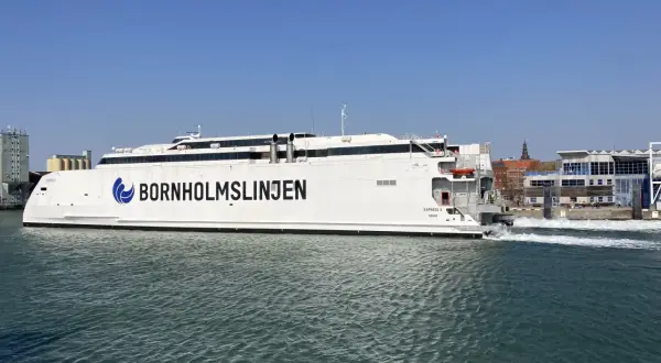 Biały prom "Bornholmslinjen Express" wypływa z portu, gotowy na podróż do Szwecji. W tle widać zabudowania portowe.