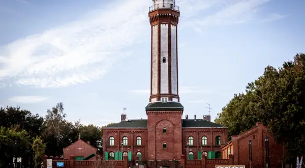 Wysoka, ceglana latarnia morska góruje nad budynkami w mieście nad Regą.