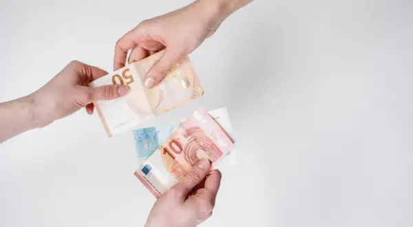 Dwie ręce przekazują sobie banknoty euro. To waluta Holandii, używana do płatności.