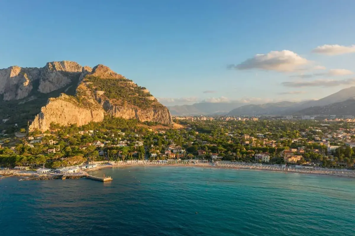 Malowniczy widok na Mondello Beach z turkusową wodą, piaszczystą plażą i górami w tle.