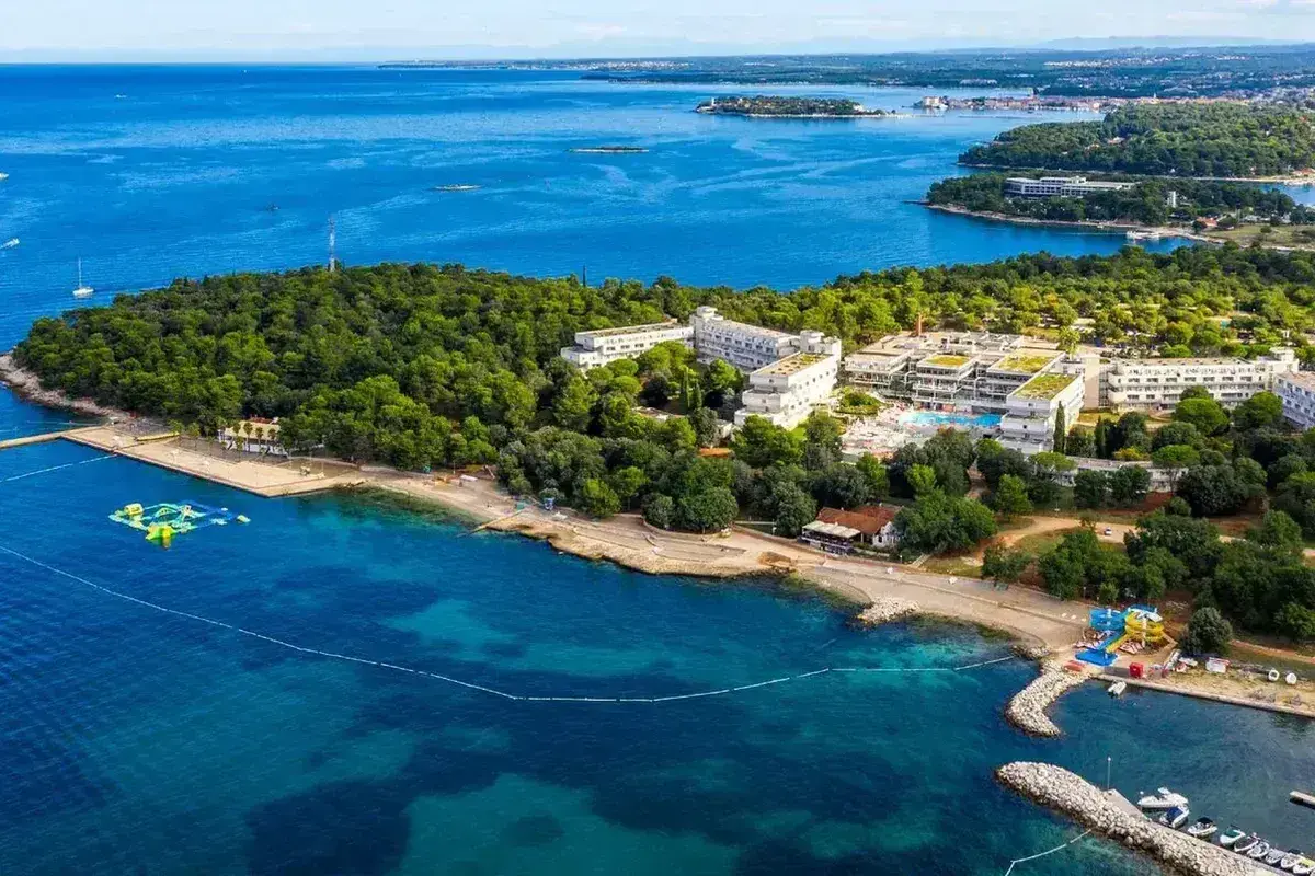 Hotel Delfin Plava Laguna, otoczony zielenią, z basenami i plażą nad turkusowym morzem. Idealne miejsce na wakacje.
