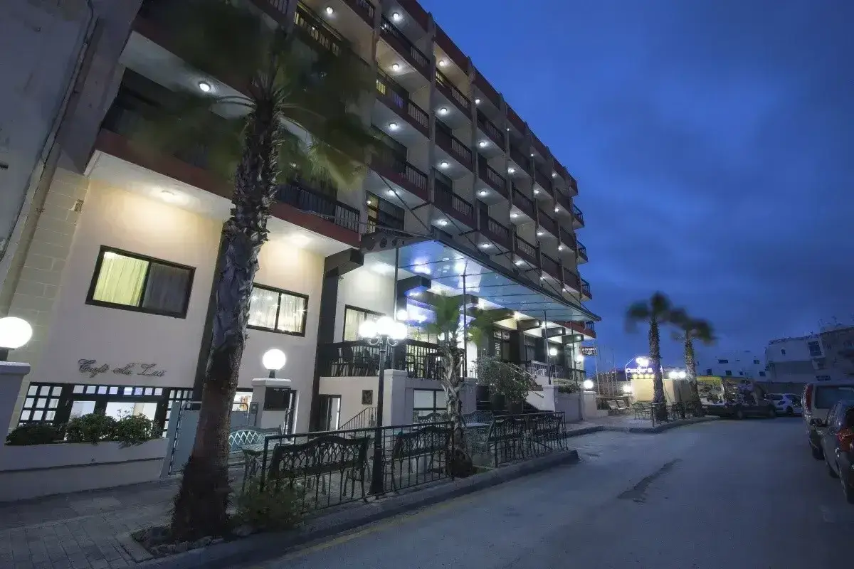 Hotel Canifor Malta o zmierzchu, z palmami i oświetlonymi balkonami.