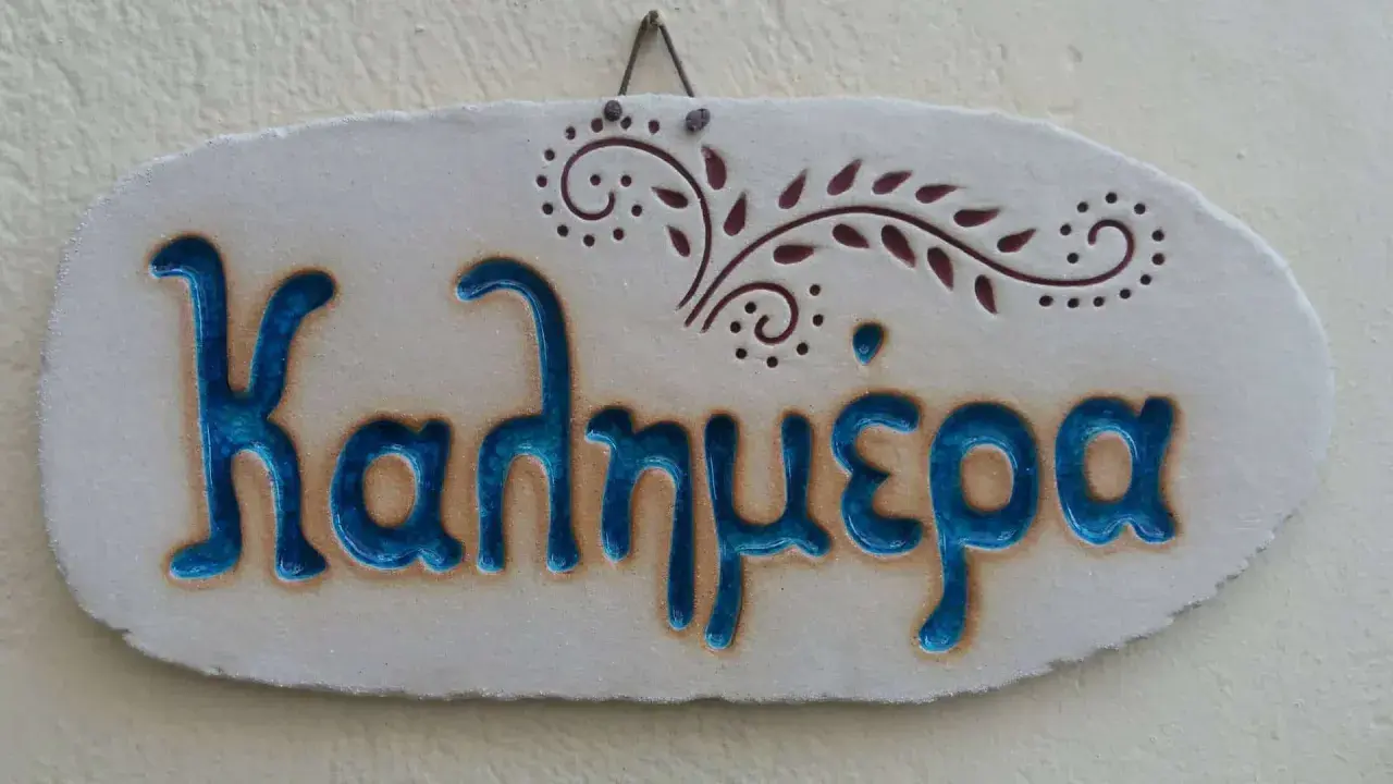 Ceramiczna tabliczka z napisem "Kalimera", czyli "cześć po grecku", ozdobiona delikatnym wzorem.