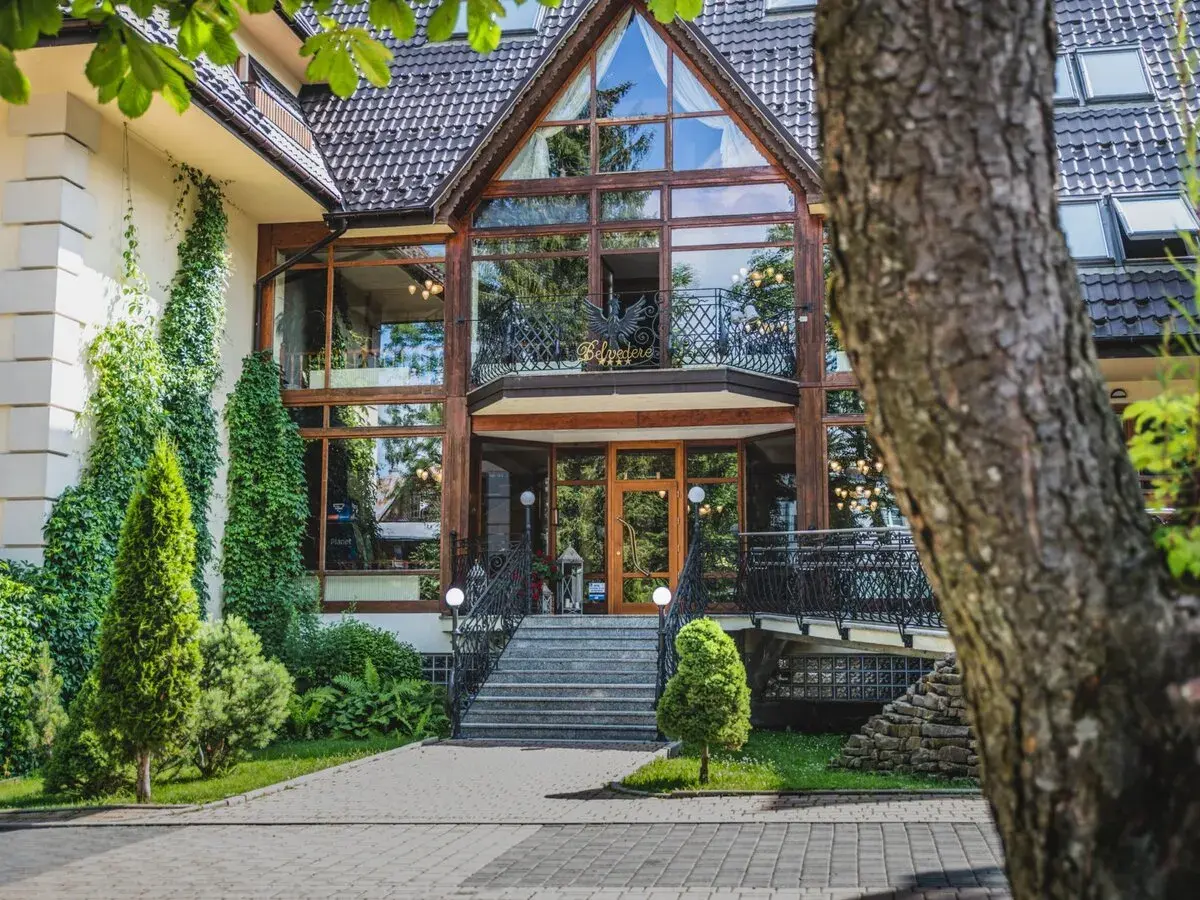 Elegancki hotel Belvedere Resort & Spa z imponującą szklaną fasadą i zielenią wokół.