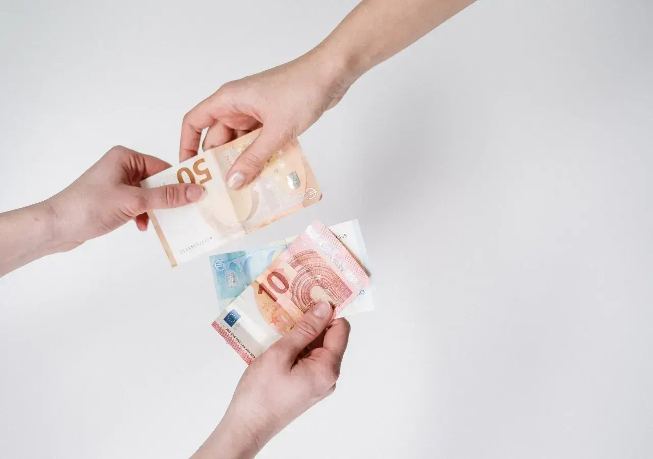 Dwie ręce przekazują sobie banknoty euro. To waluta Holandii, używana do płatności.
