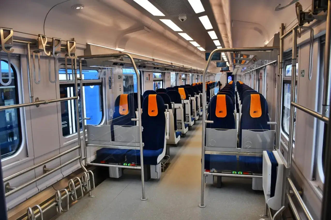 Wnętrze nowoczesnego wagonu bezprzedziałowego PKP Intercity. Rzędy granatowych siedzeń z pomarańczowymi zagłówkami, poręcze i przegrody.