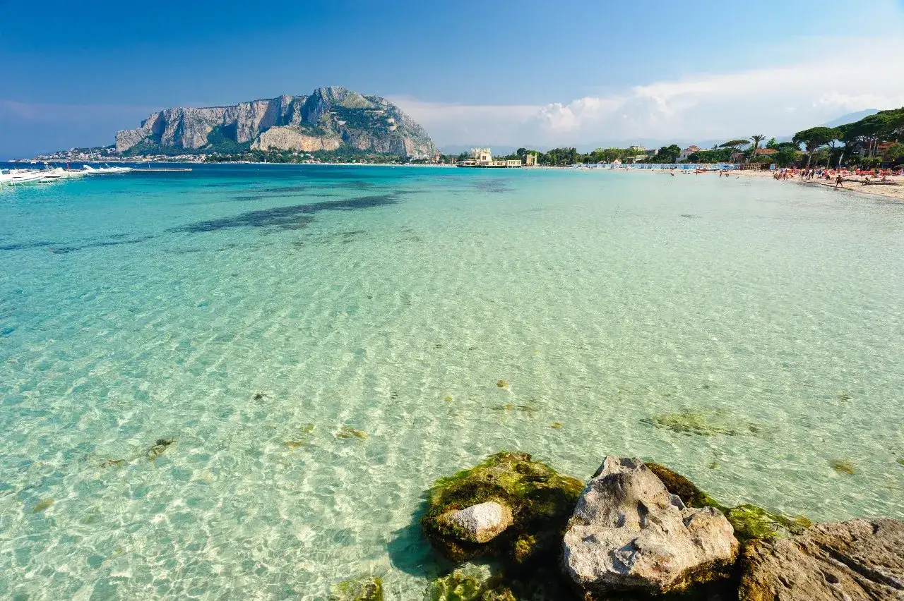 Czysta, turkusowa woda na plaży Mondello, z łagodnymi falami i widokiem na górzysty krajobraz w oddali.