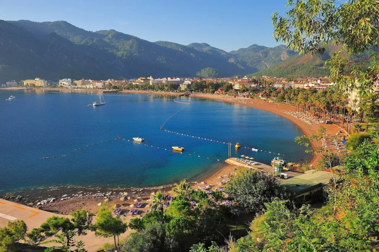 Piękna zatoka z plażą i palmami w Kusadasi. Idealna pogoda w październiku, błękitne morze i góry w tle.
